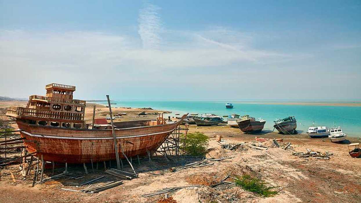 A view of old rusty ships and boats on the shores of a beach with turquoise water in the background