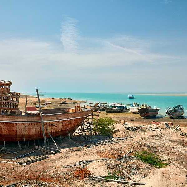 A view of old rusty ships and boats on the shores of a beach with turquoise water in the background