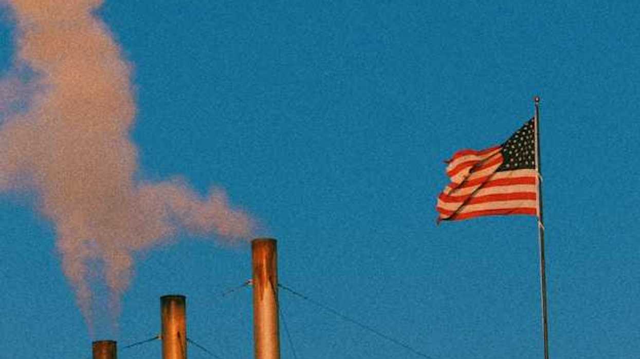 A view of smokestacks spewing pollution into the air with an American flag flying nearby
