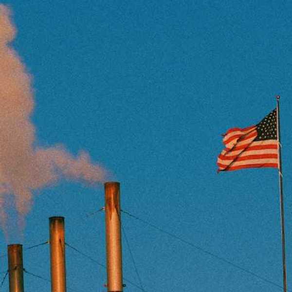 A view of smokestacks spewing pollution into the air with an American flag flying nearby