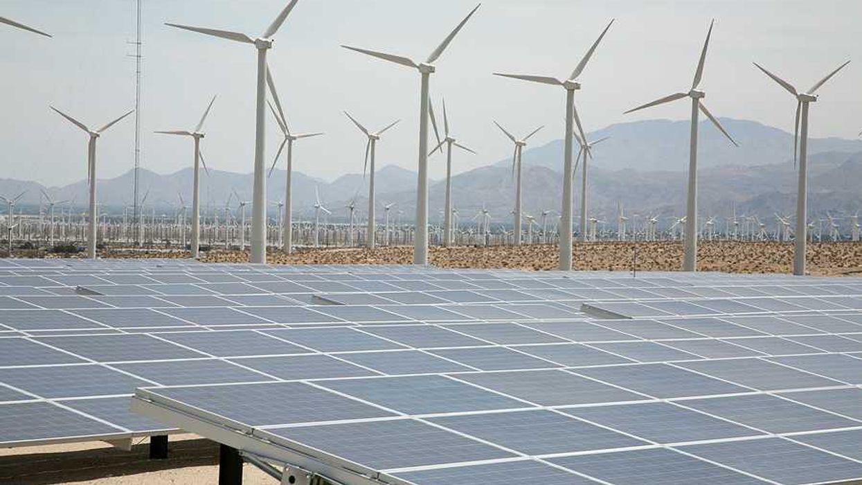 A view of solar panels and wind turbines with mountains in the background