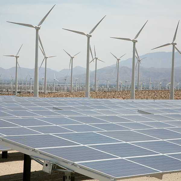 A view of solar panels and wind turbines with mountains in the background