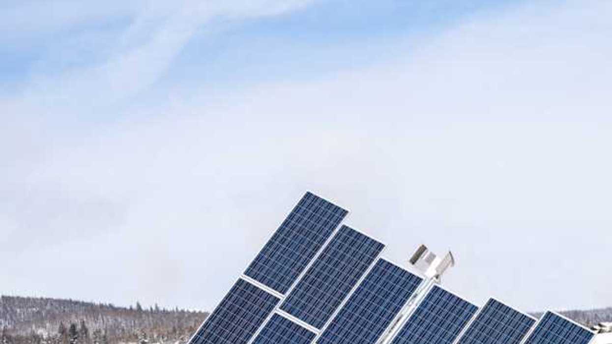 A view of solar panels with snow-covered hills behind them