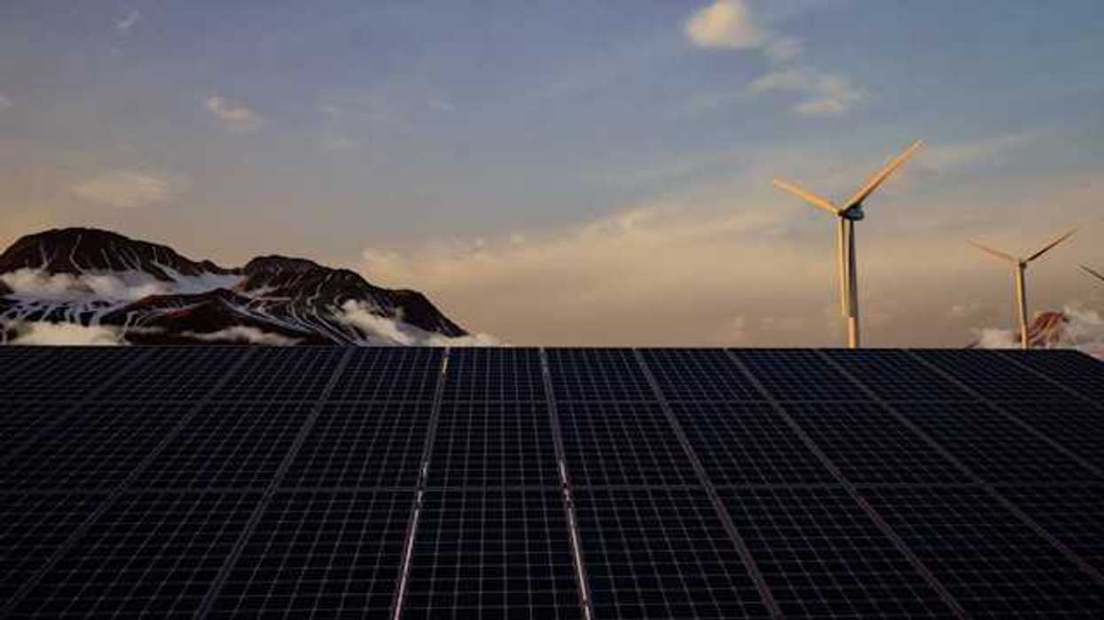 A view of solar panels with wind turbines and mountains in the background