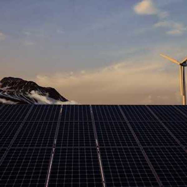 A view of solar panels with wind turbines and mountains in the background