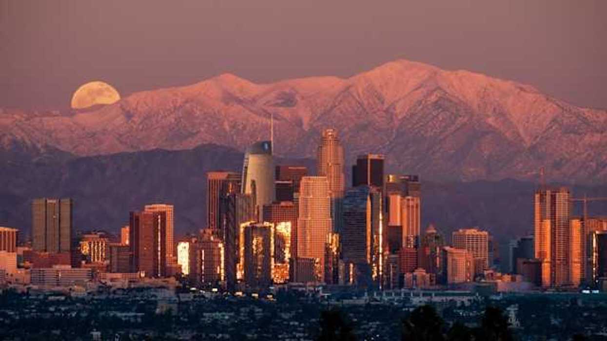 A view of the Denver skyline at dusk with the moon rising behind the mountains
