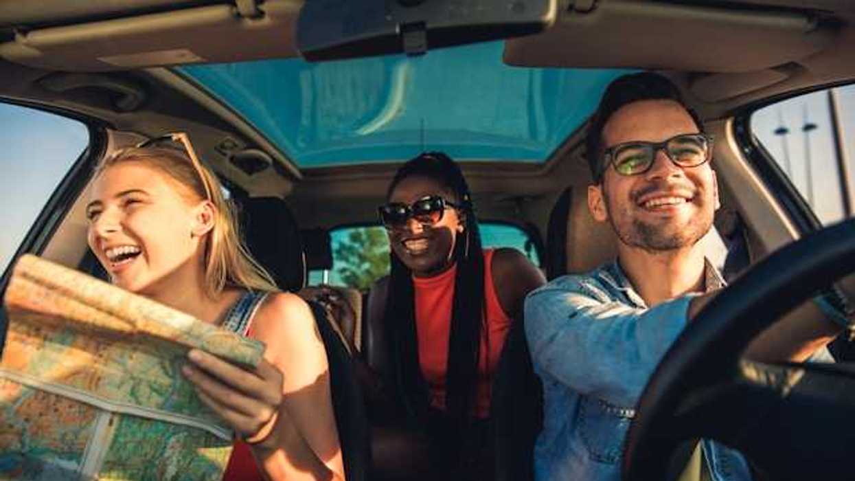 A view of the interior of a car with three laughing people, one of whom is looking at a map