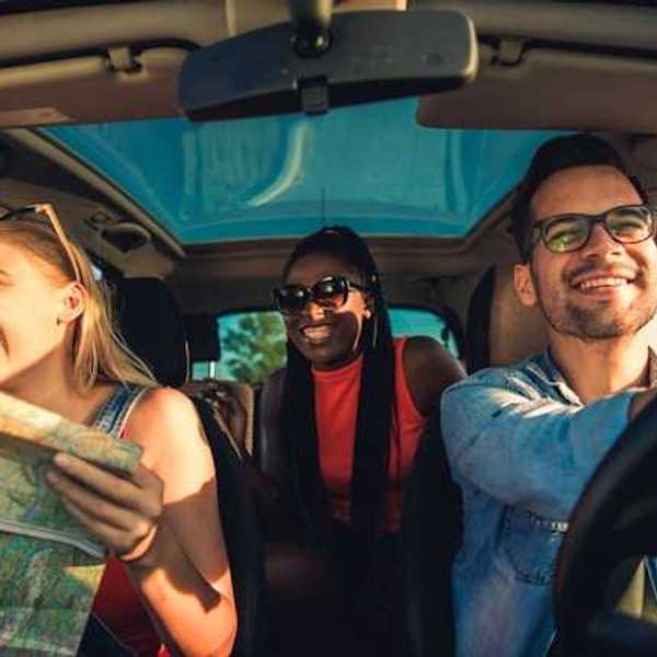 A view of the interior of a car with three laughing people, one of whom is looking at a map