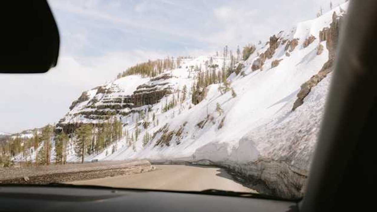 A view out of a car at a mountain road with snowy hillsides