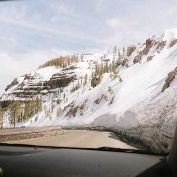 A view out of a car at a mountain road with snowy hillsides