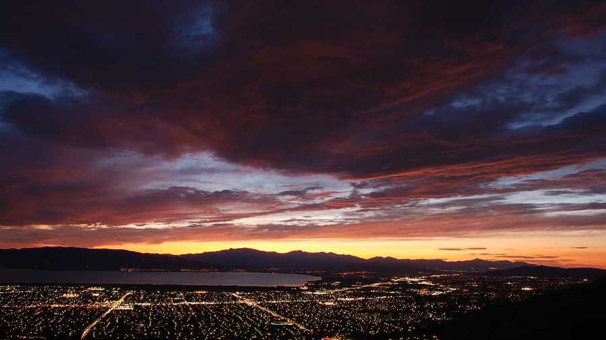 A view over a darkened valley with the lights of houses and a lake in the background