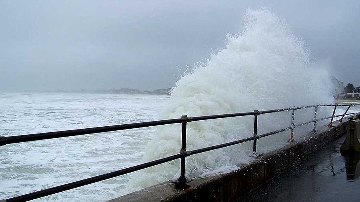 A wave coming up against a fenced sea wall during a storm