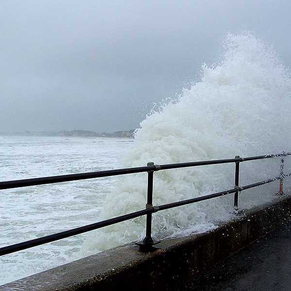A wave coming up against a fenced sea wall during a storm