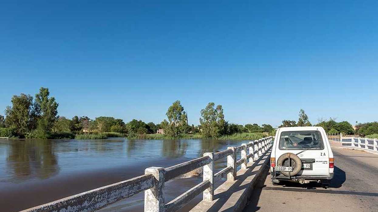A white car parked on a bridge with rising flood waters beneath it