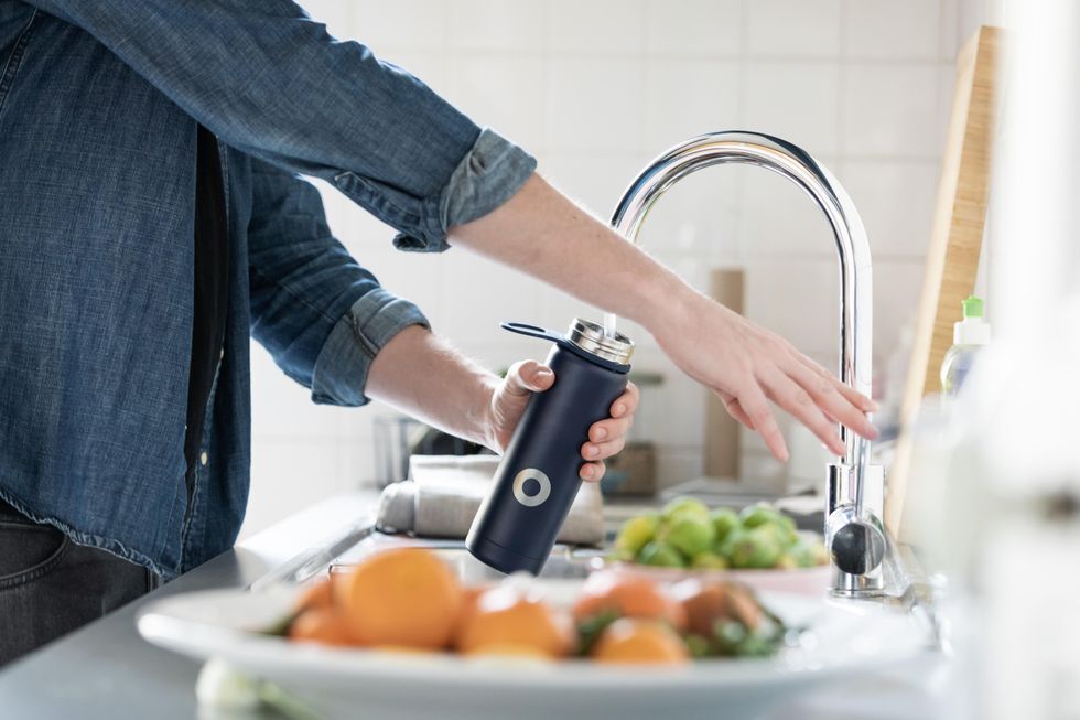 a white person fills a reusable metal water bottle at the sink.