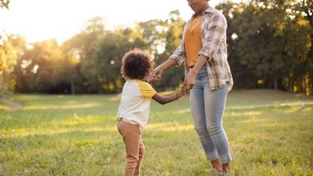 A woman and a child holding hands and dancing in a field