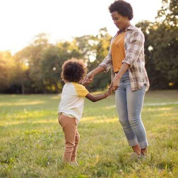 A woman and a child holding hands and dancing in a field