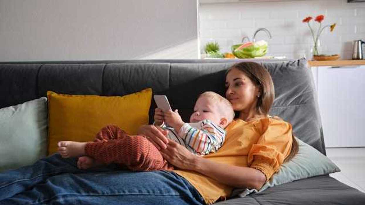 A woman and baby are lying on a grey sofa