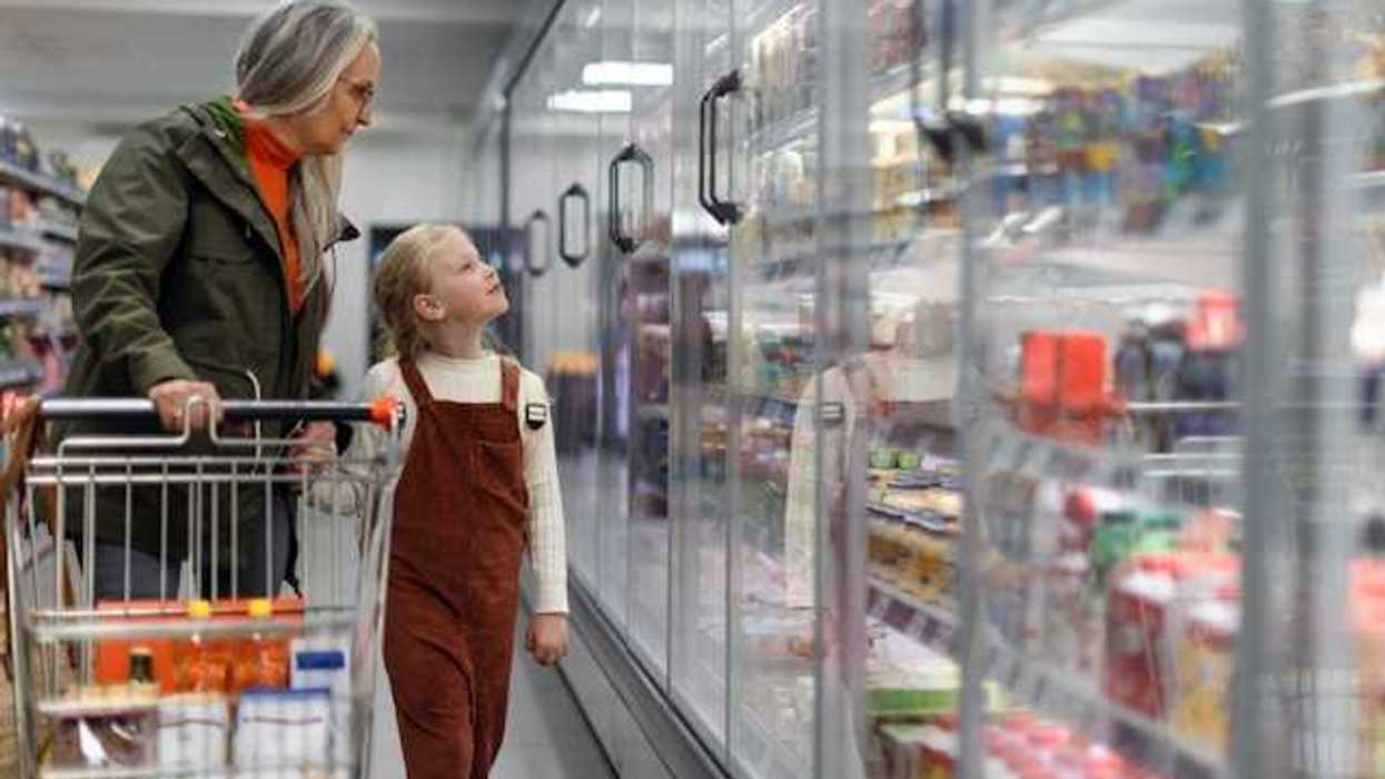 A woman and child standing in front of grocery store refrigerators
