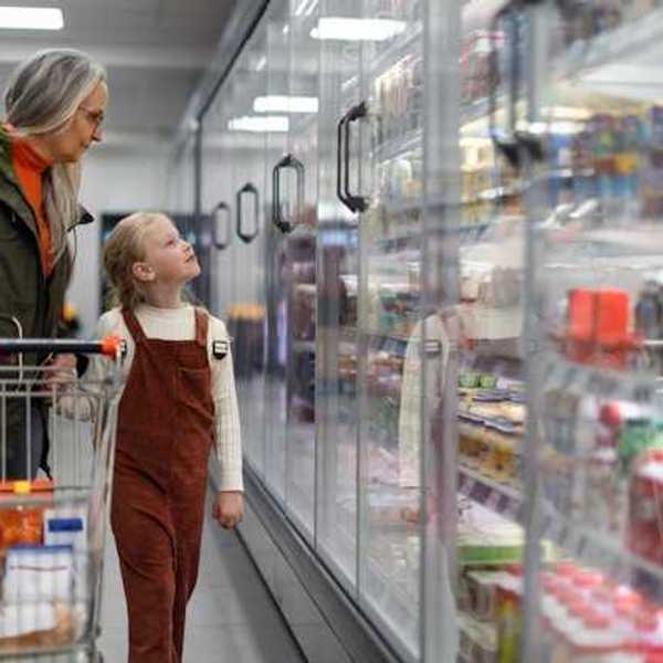 A woman and child standing in front of grocery store refrigerators