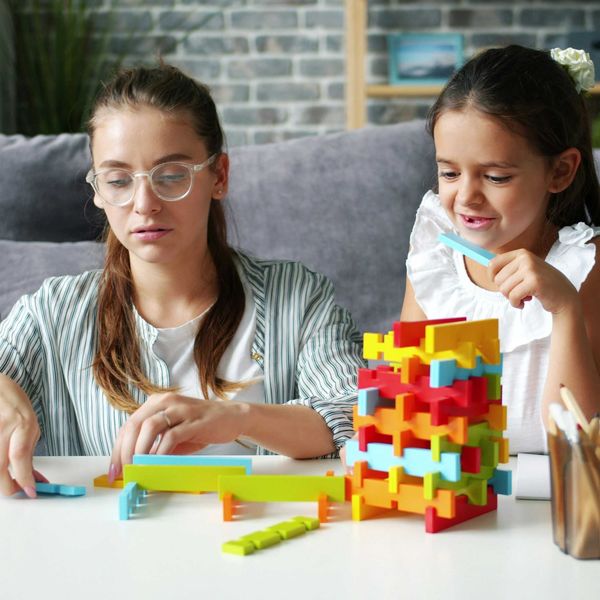 A woman and little girl building with colorful blocks at a table.