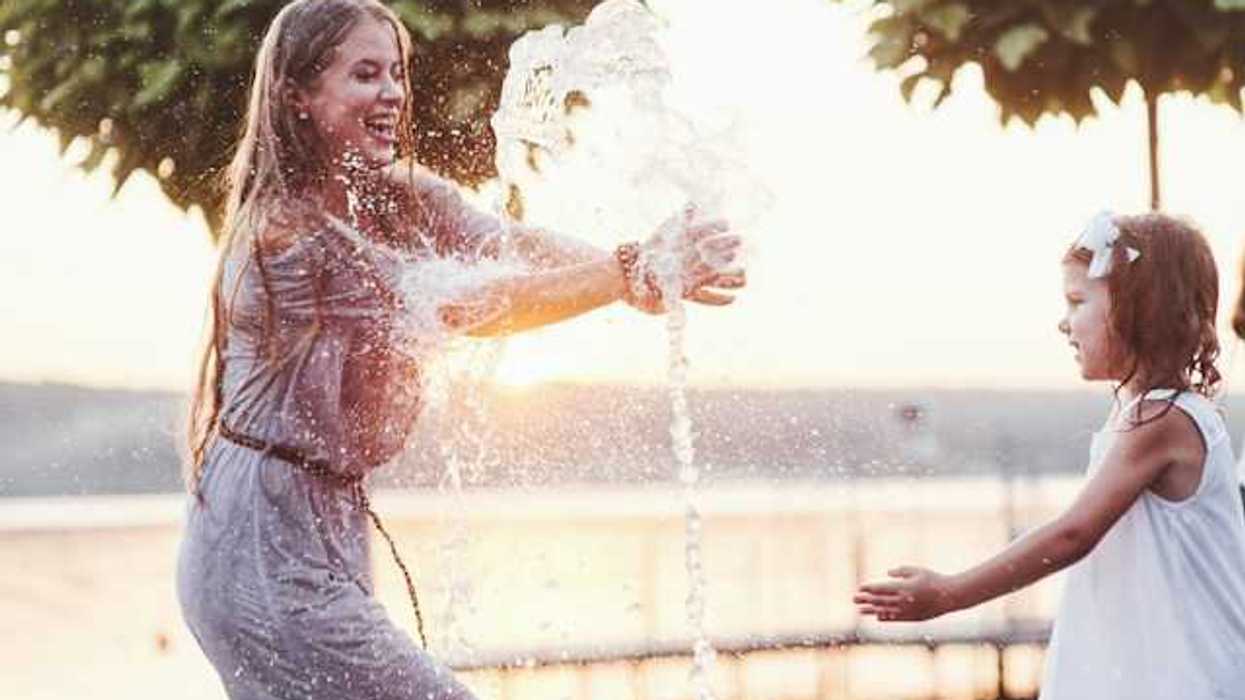 A woman and little girl playing in a water fountain