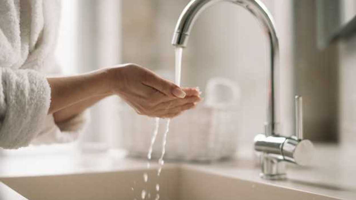A woman cupping her hands under water coming out of a kitchen sink