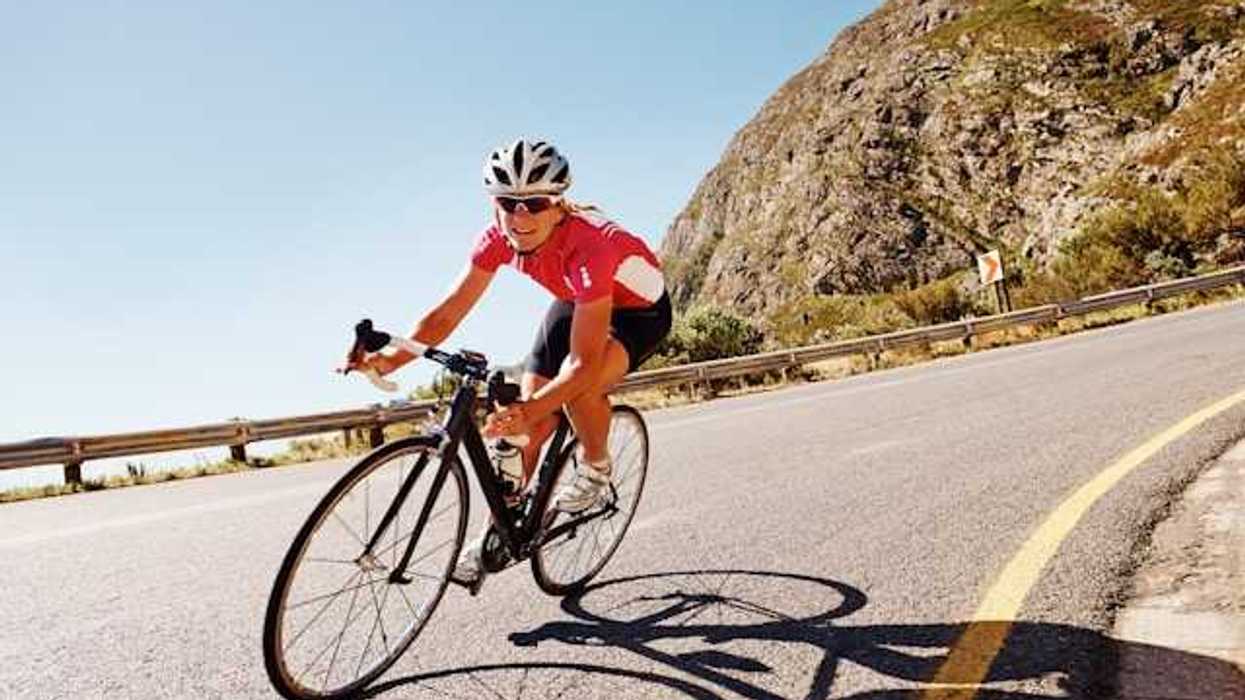 A woman cycling down a road in the sunshine with a red bike kit on
