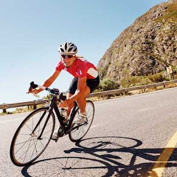 A woman cycling down a road in the sunshine with a red bike kit on