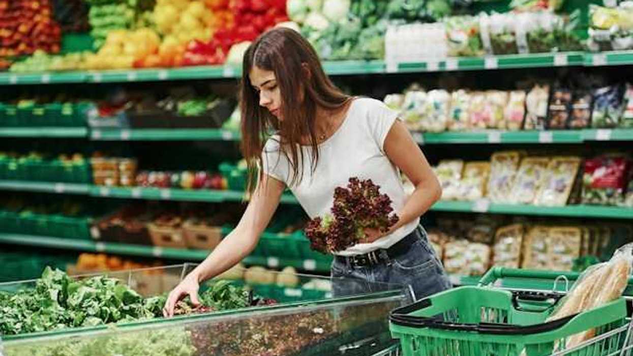 A woman grabbing lettuce in produce section of a grocery store