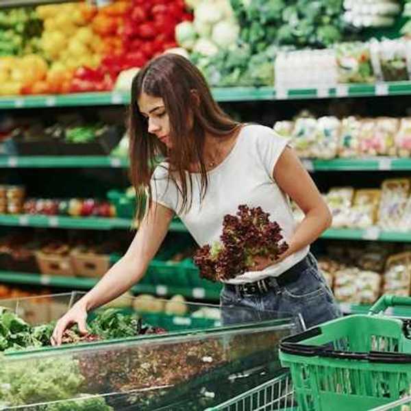 A woman grabbing lettuce in produce section of a grocery store