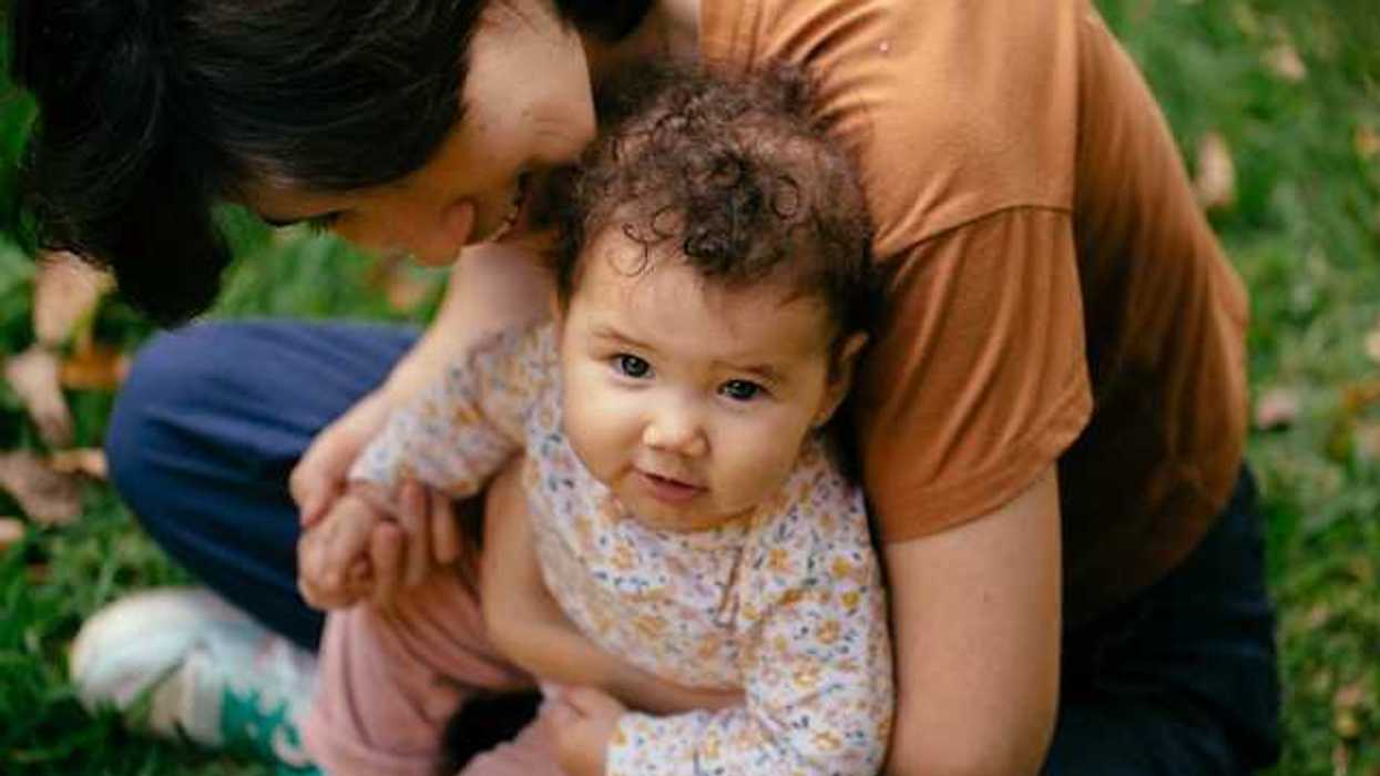 A woman holding a baby in her arms while sitting on the grass