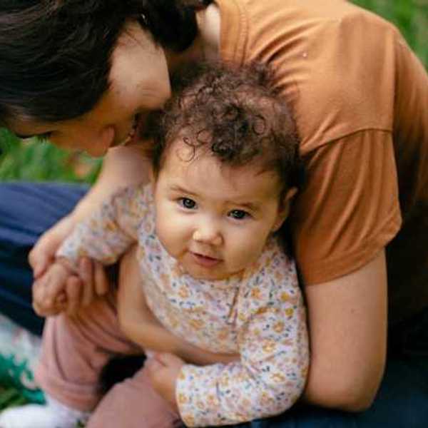 A woman holding a baby in her arms while sitting on the grass