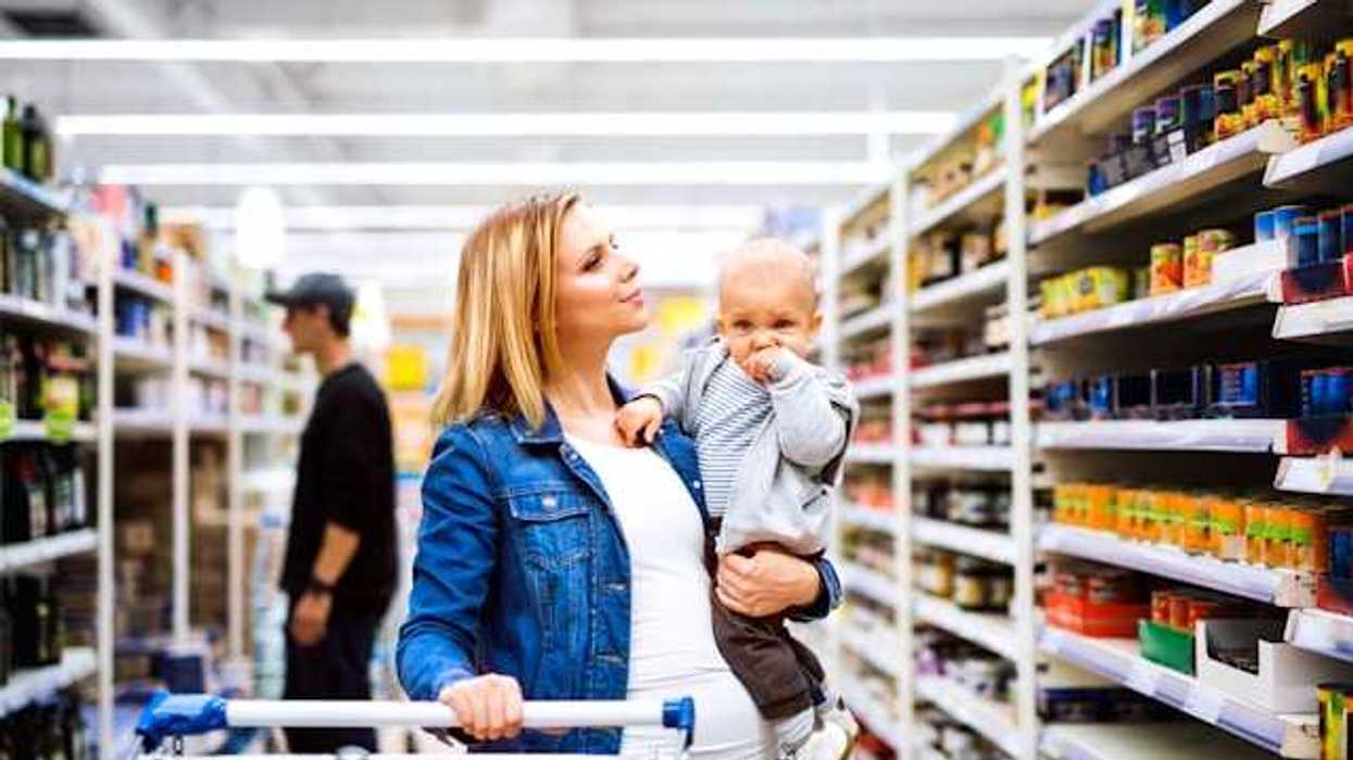 A woman holding a baby walking down a grocery store aisle