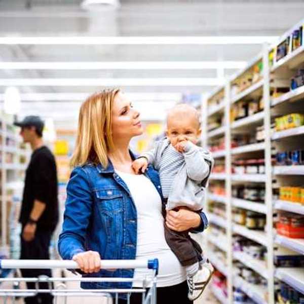 A woman holding a baby walking down a grocery store aisle