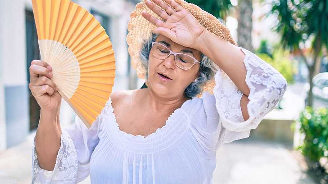 A woman holding a fan and holding her hand to her forehead on a hot day