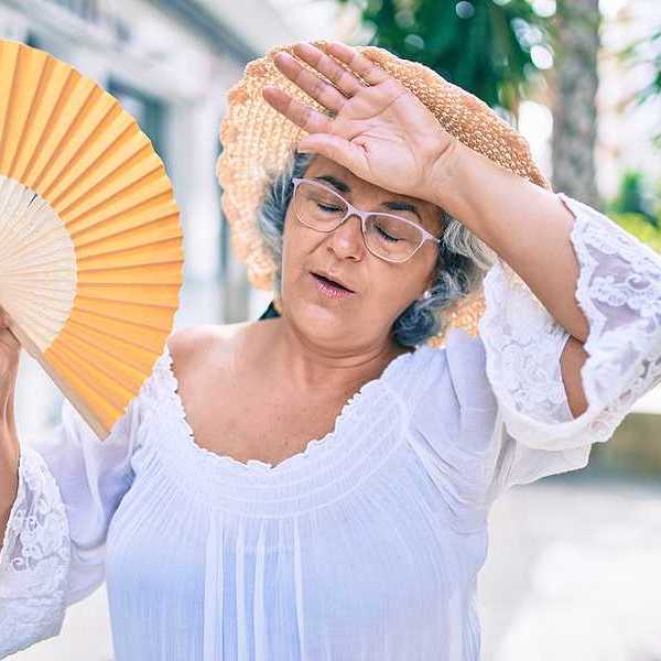 A woman holding a fan and holding her hand to her forehead on a hot day