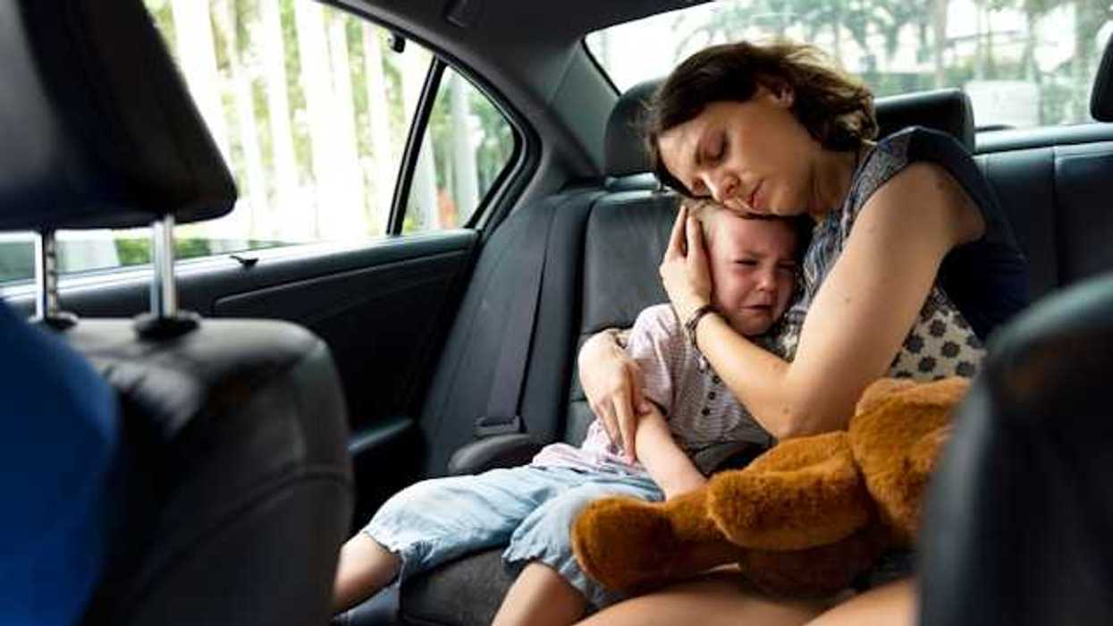 A woman hugging a crying child in the back of a car