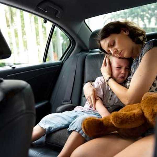 A woman hugging a crying child in the back of a car