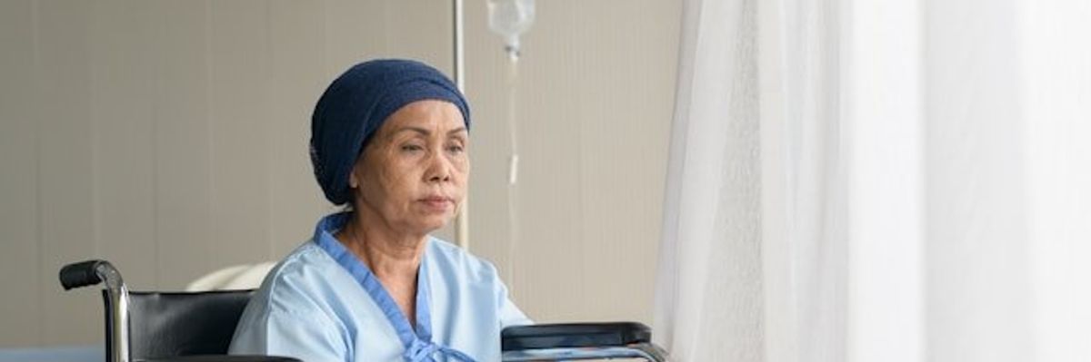 A woman in a hospital gown sitting in a wheelchair with an IV bag next to her.