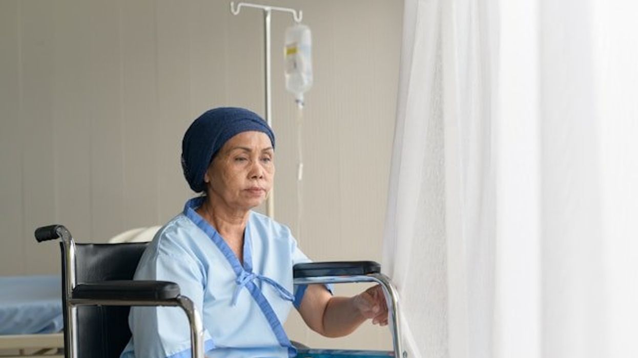 A woman in a hospital gown sitting in a wheelchair with an IV bag next to her.