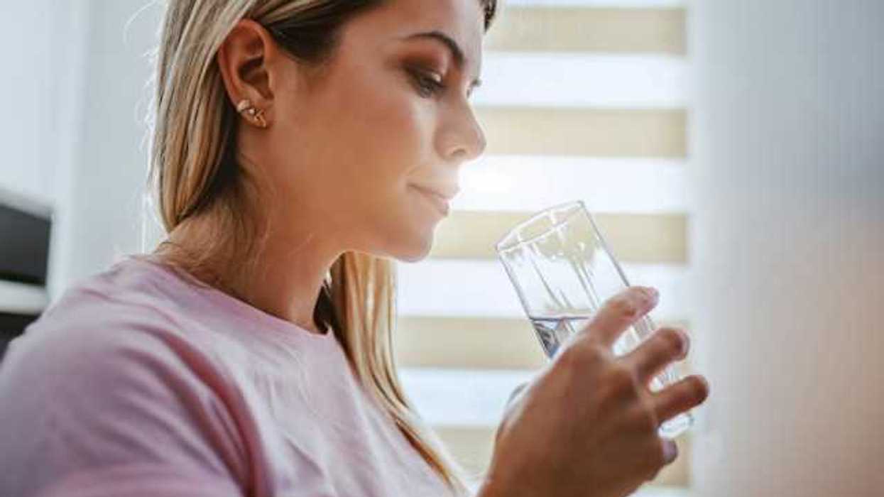 A woman in a pink shirt drinking water out of a glass