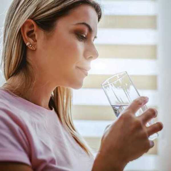 A woman in a pink shirt drinking water out of a glass