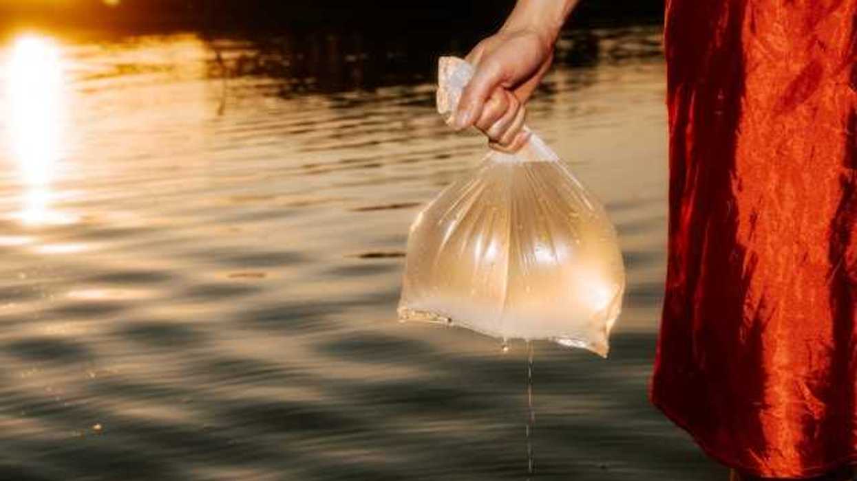 A woman in a red skirt holding a plastic bag full of water