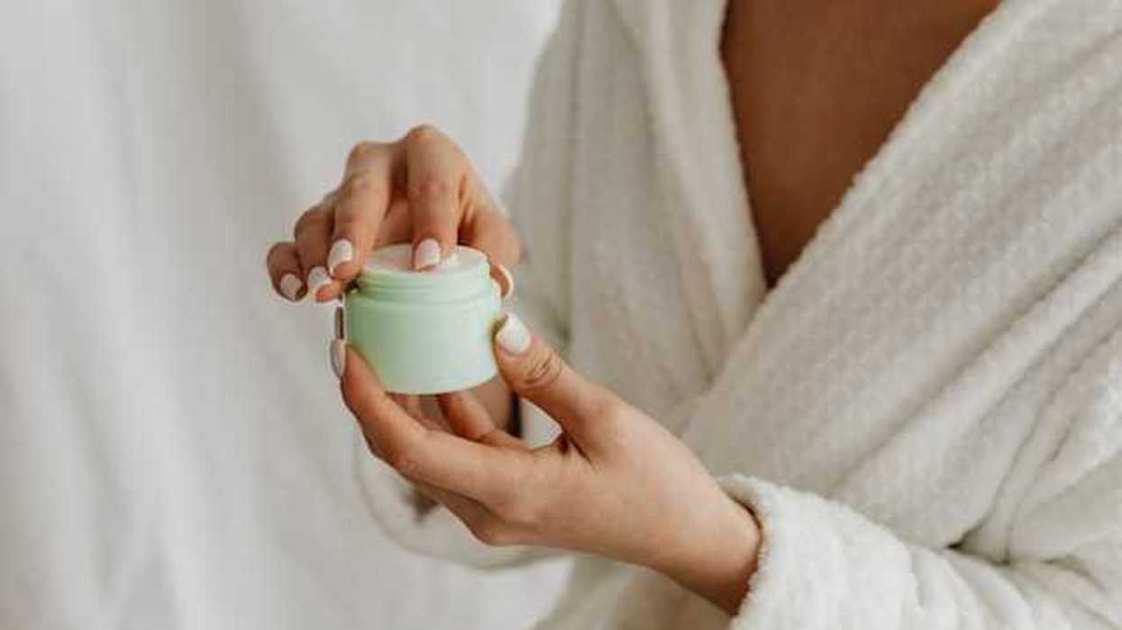 A woman in a robe holding a green plastic container with skin cream in it