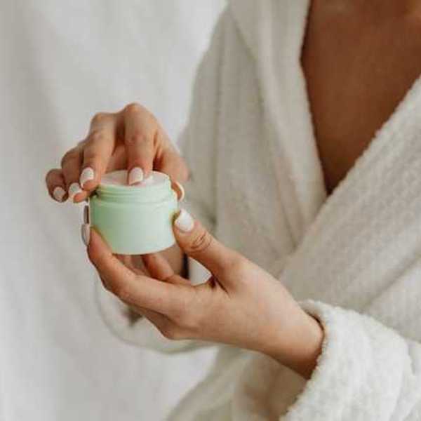 A woman in a robe holding a green plastic container with skin cream in it