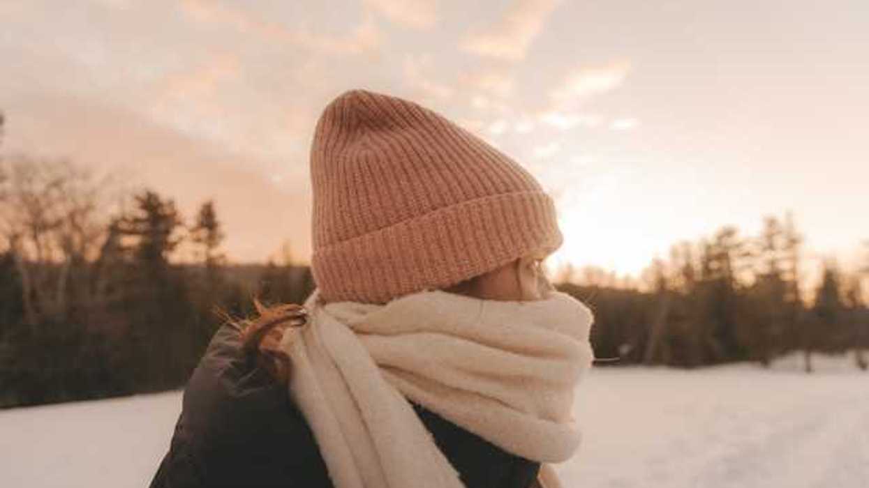A woman in a snowy lanscape wearing a hat and scarf bundled against the cold weather