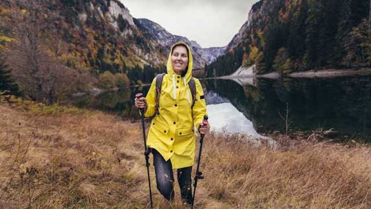 A woman in a yellow raincoat hiking near a beautiful lake