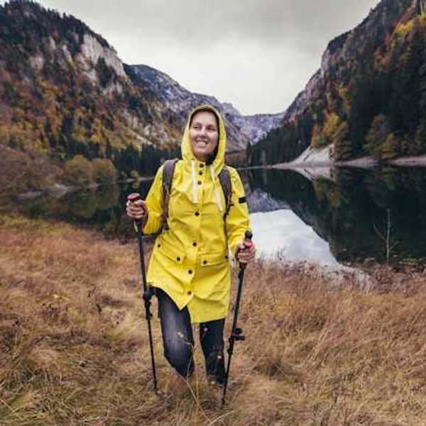A woman in a yellow raincoat hiking near a beautiful lake