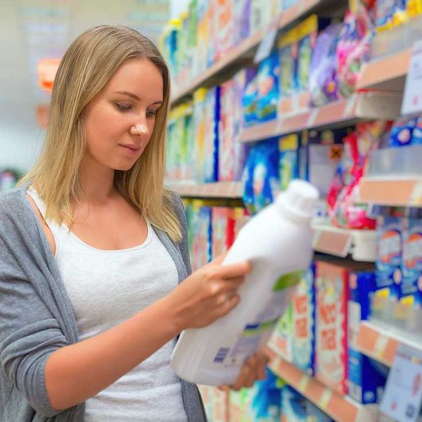 A woman looking at the label on a plastic bottle of laundry detergent